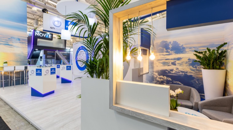 Espace détente d’un stand avec fauteuils, plantes et suspensions lumineuses