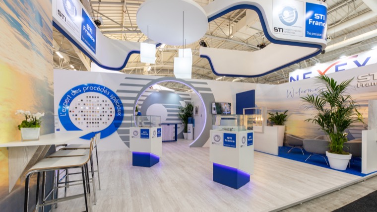 Stand blanc et bleu avec arche lumineuse, vitrines sur socles bleus et espace bar