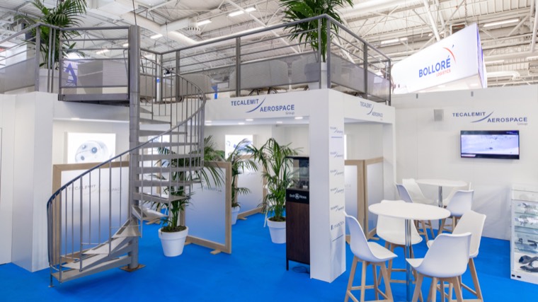 Stand blanc sur moquette bleue avec escalier en colimaçon menant à une mezzanine
